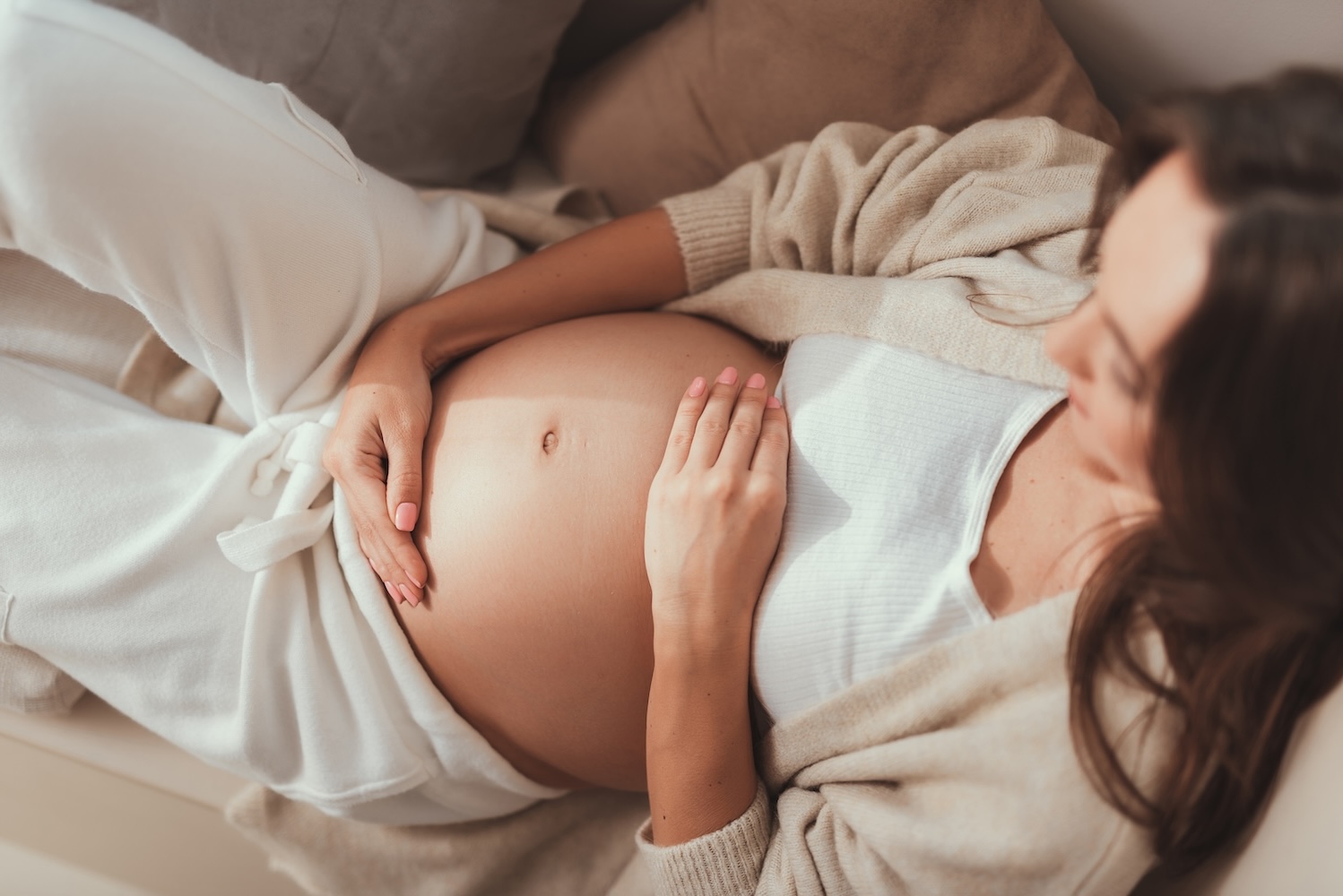 803c2f_b9dfb44353f74442b066619b291b1cf0_mv2 Pregnant lady lying and holding her hands on pregnant belly